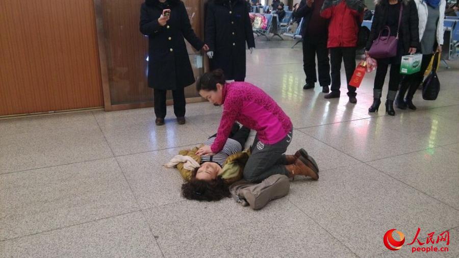 2月27日，沈陽市火車站候車室內，賈大媽突發心肌梗塞昏迷。沈陽軍區總醫院醫生李偉（穿粉衣者）上前相救。