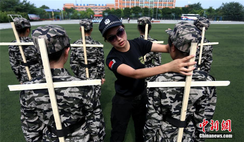 炎炎烈日下，參加軍訓的學子們頭頂礦泉水瓶，手挂水壺，身背十字木條，衣領口別扑克牌站軍姿列隊。張鑫 攝