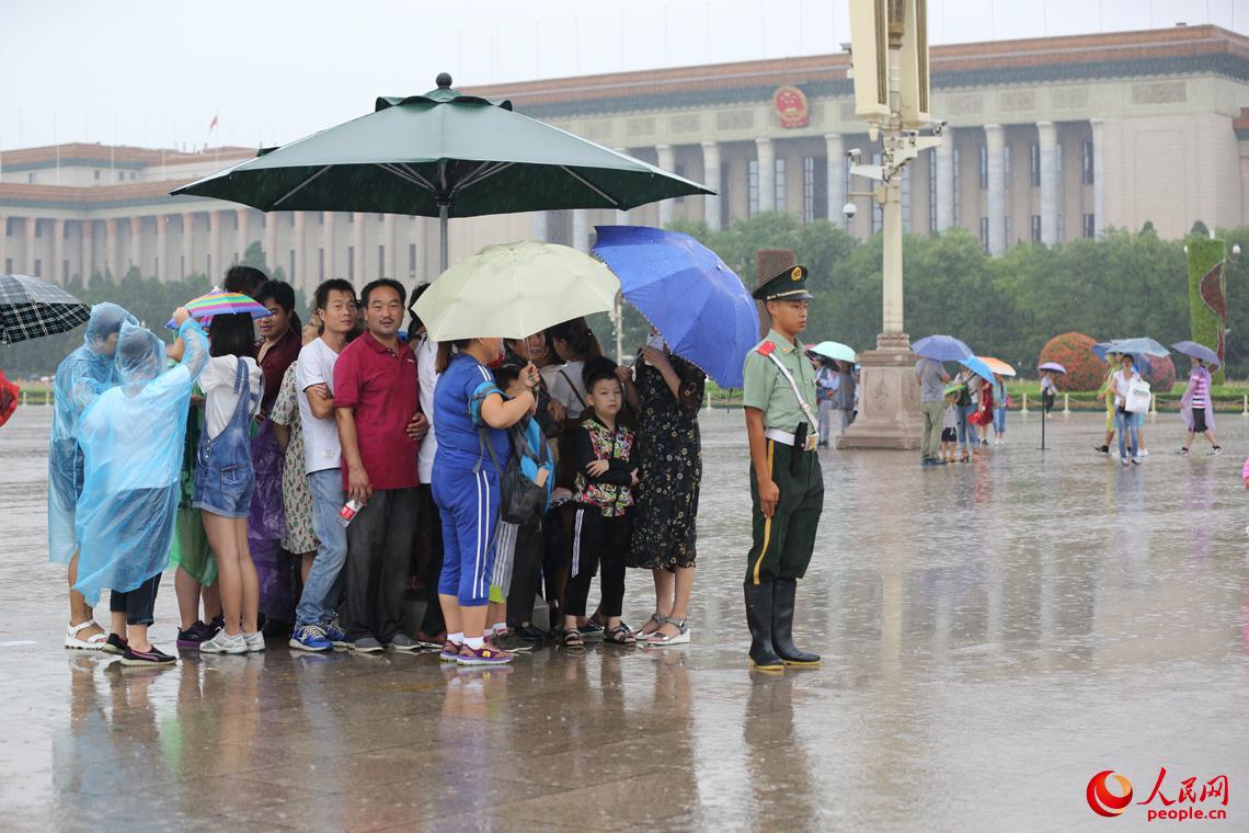 天安门广场执勤哨兵将雨中岗伞让给群众。王彦高摄