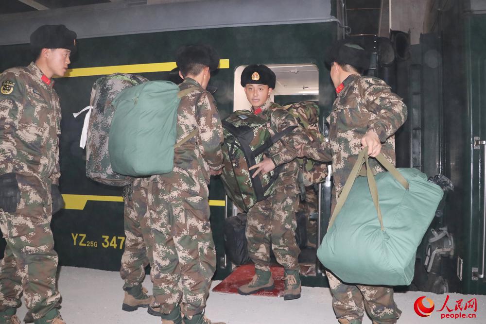 下火車時，一名新兵前抱后背，班長和戰友在一旁接過行李。