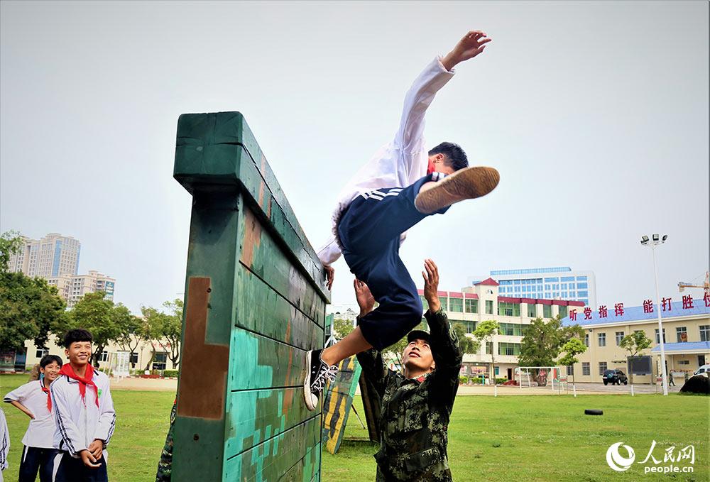 一名学生在武警官兵的保护下体验翻越高墙。