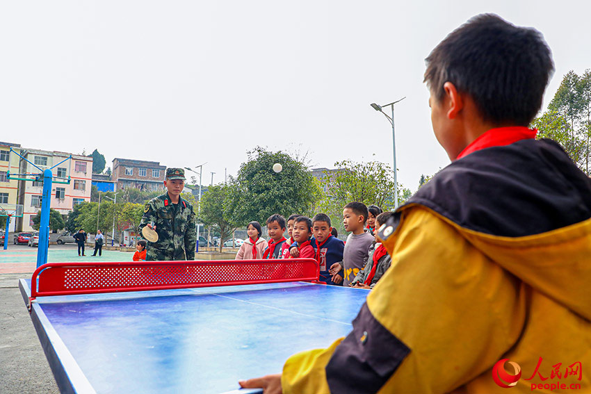 武警官兵与学生一起打乒乓球。