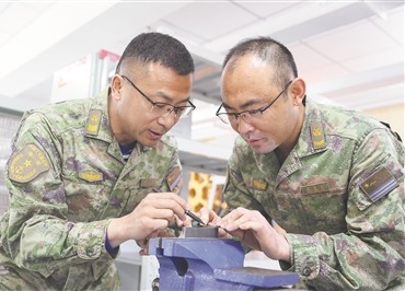一級軍士長趙三雷（左）與張慶山探討鉗工工藝。